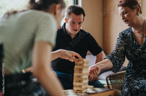 A boy with Down syndrome, a girl in a wheelchair, and an elderly woman enjoying a building blocks game together, fostering friendship and inclusion. photo