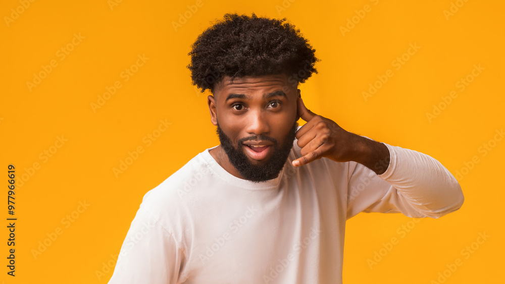 Handsome single man making call me sign with hand shaped like phone, orange background, copy space Handsome single man making call me sign with hand shaped like phone, orange background, copy space