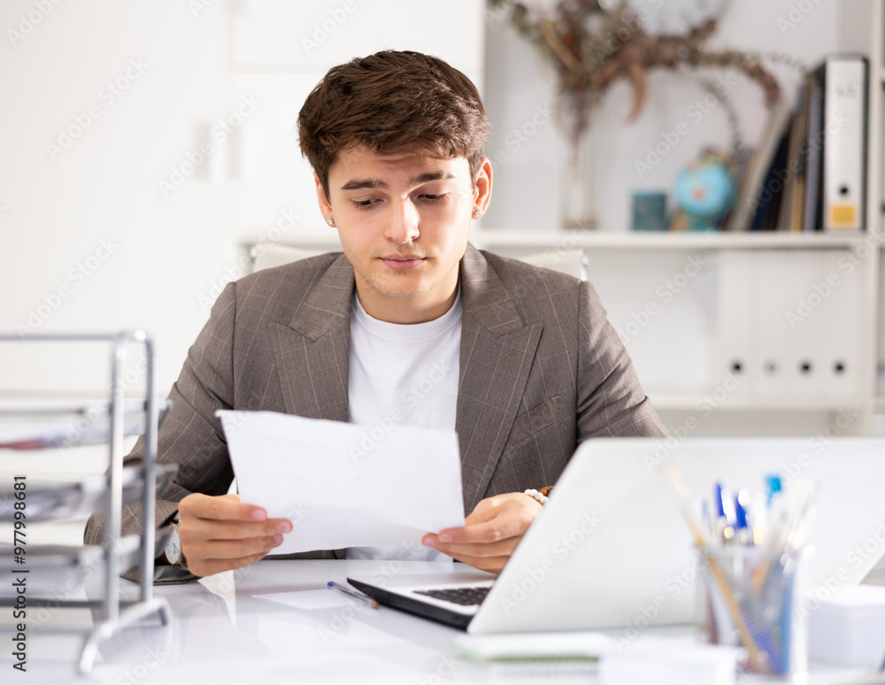 Obraz premium Male bookkeeper doing paperwork in his workplace in office - checks accounting documents