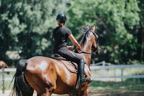 Fototapeta Woman riding a horse in an outdoor equestrian arena, enjoying a sunny day surrounded by nature