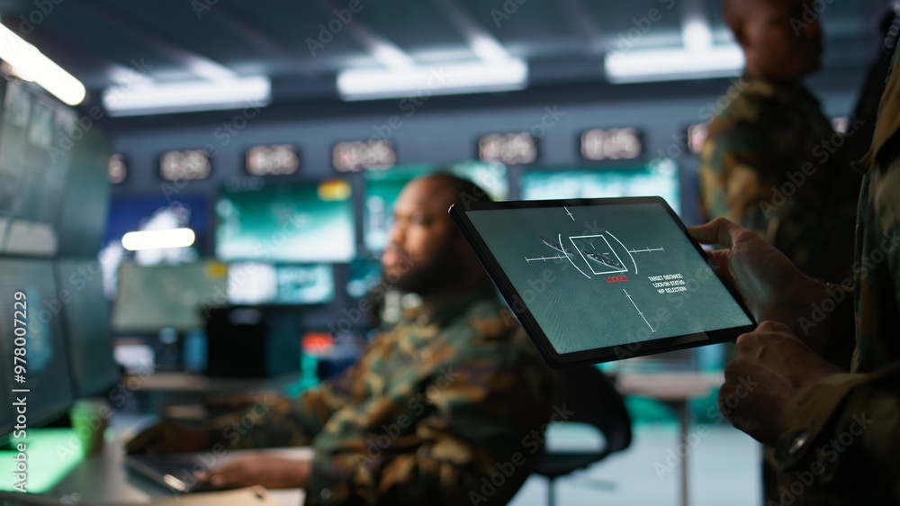 Obraz premium Military agent working in control room, using software on tablet, analyzing aerial reconnaissance data. Close up of intelligence corps expert controlling drones with portable device, camera B