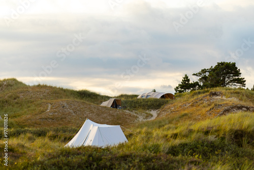 Campsite nestled in rolling dunes at sunset with tents and greenery on a tranquil evening photo