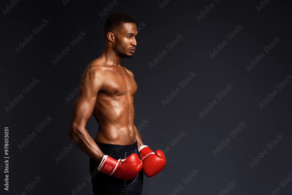 Fighter. Half-turned athletic black man in boxing gloves looking aside at copyspace isolated over black studio wall Fighter. Half-turned athletic black man in boxing gloves looking aside at copyspace isolated over black studio wall