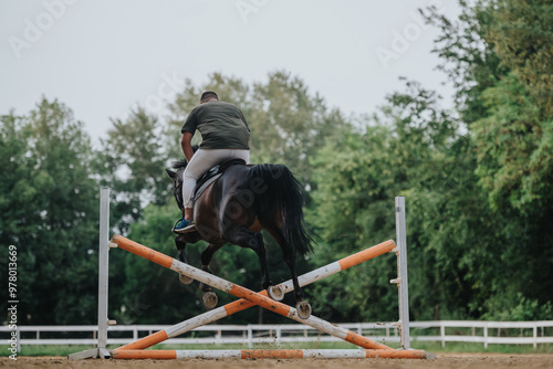 Equestrian riding horse jumps over an obstacle in an outdoor training arena. Experience the adrenaline of horse and rider in mid-air action.