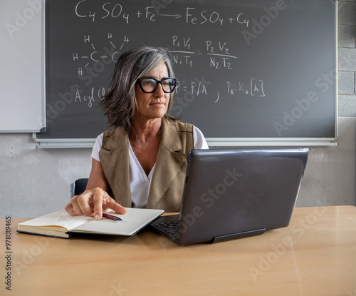 Middle-aged female teacher working with a notebook and a laptop in a high school or university. Science teacher