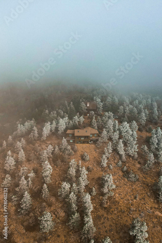 A foggy aerial view of a secluded cabin surrounded by snow-covered trees. Ideal for outdoor lifestyle, nature retreats, and winter-themed editorial or travel content.