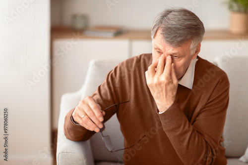 Eyes Fatigue. Senior Man Massaging Nosebridge Sitting On Sofa At Home. Selective Focus, Free Space photo