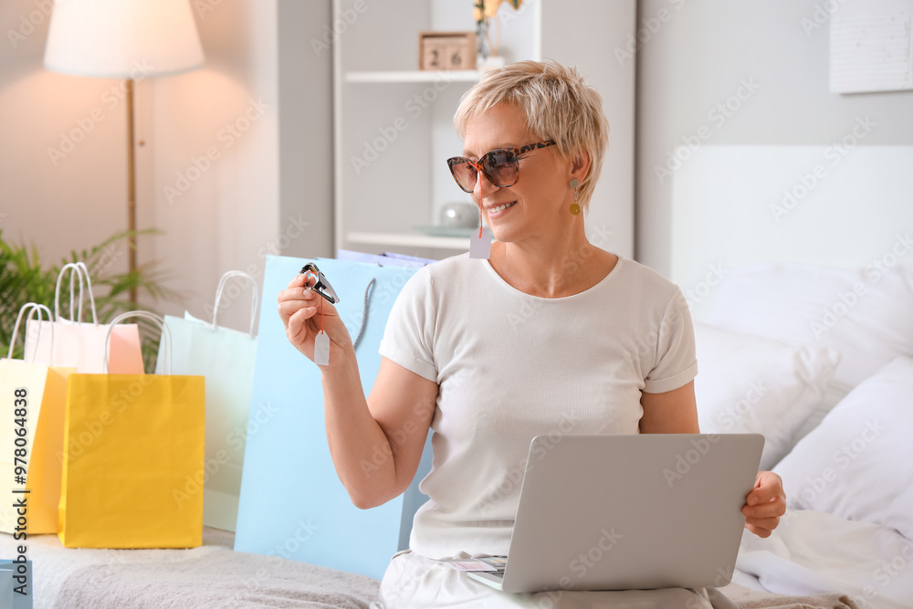 Mature woman with new sunglasses and laptop in bedroom. Online shopping Mature woman with new sunglasses and laptop in bedroom. Online shopping