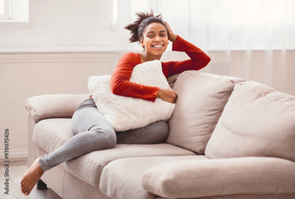 Enjoying Weekend. Relaxed Afro Lady Sitting On Couch Hugging Pillow And Smiling Indoor. Free Space Enjoying Weekend. Relaxed Afro Lady Sitting On Couch Hugging Pillow And Smiling Indoor. Free Space
