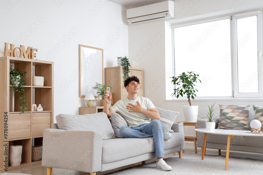 Young man resting on sofa in room with operating air conditioner Young man resting on sofa in room with operating air conditioner