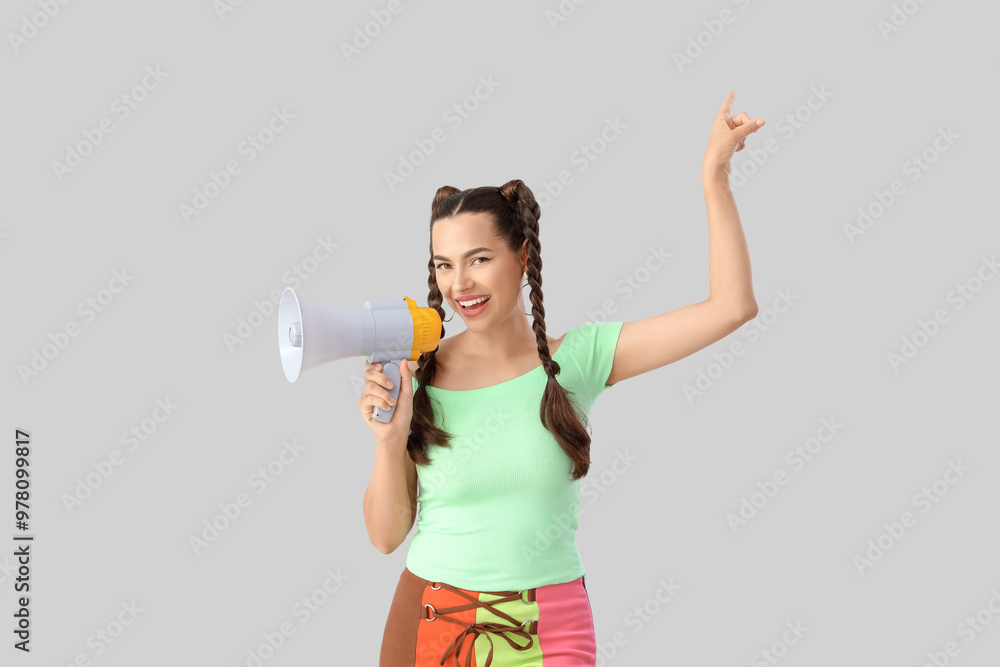 Beautiful young happy woman with braids holding megaphone and pointing at something on grey background Beautiful young happy woman with braids holding megaphone and pointing at something on grey background
