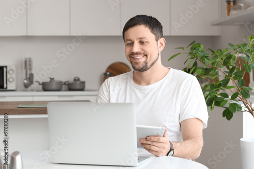 Young male teacher with laptop and notebook giving online lesson at home