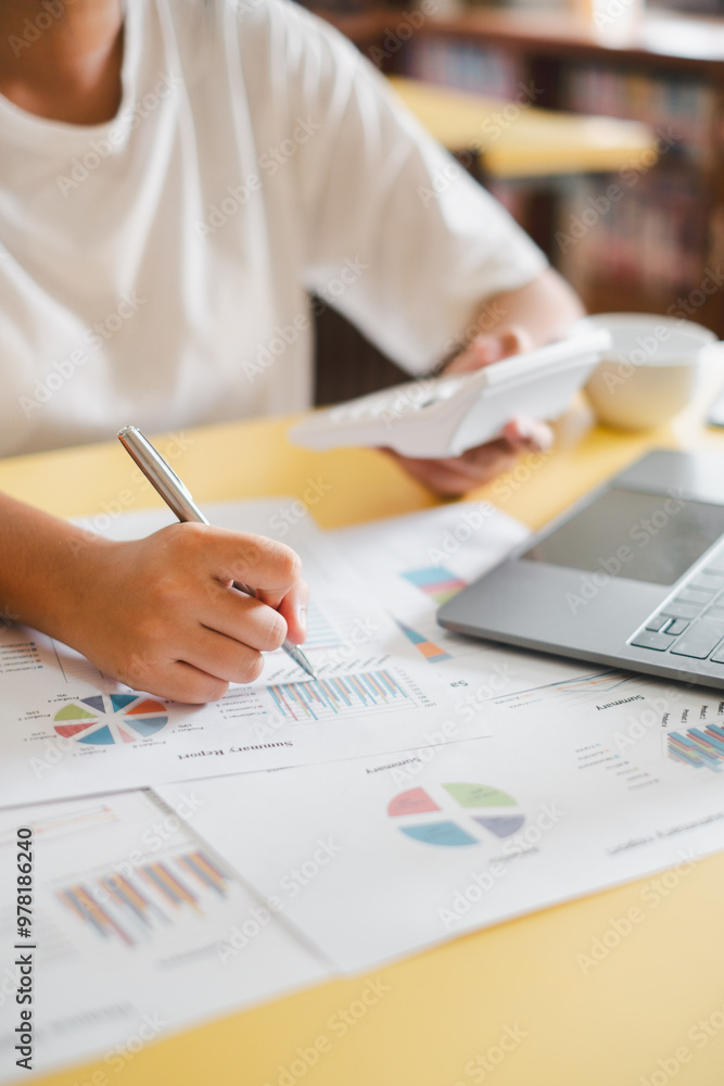Close-up of a business professional analyzing financial data with charts and graphs on a desk, using a calculator and laptop. Close-up of a business professional analyzing financial data with charts and graphs on a desk, using a calculator and laptop.