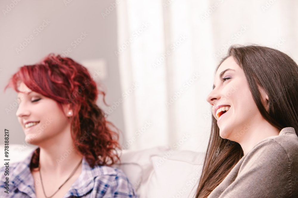 Two young women laughing together on the couch at home Two young women laughing together on the couch at home