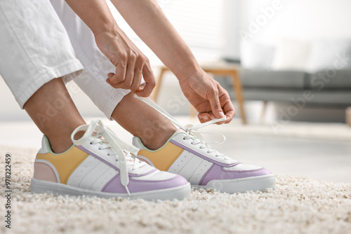 Woman tying shoelace of sneaker indoors, closeup