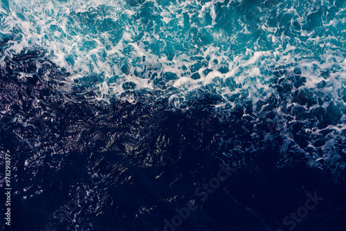 Aerial shot capturing the contrast between dark ocean waves and bright white seafoam, creating dynamic and dramatic seascape. Backgrounds or marine themes
