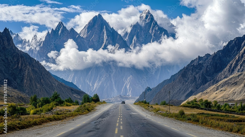 Clouds hovering over the jagged peaks of Passu Cones as a paved road meanders through the Karakoram Highway, a tranquil route in Hunza Valley.