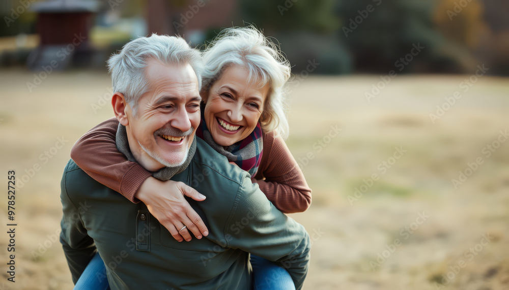 A joyful older couple enjoys a playful moment outdoors, embracing life together with smiles in a natural setting. A joyful older couple enjoys a playful moment outdoors, embracing life together with smiles in a natural setting.