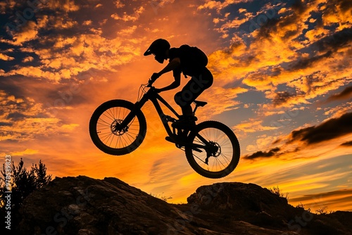 At dusk, a mountain biker silhouette leaps across rugged terrain, capturing the essence of extreme sports and adventure photo