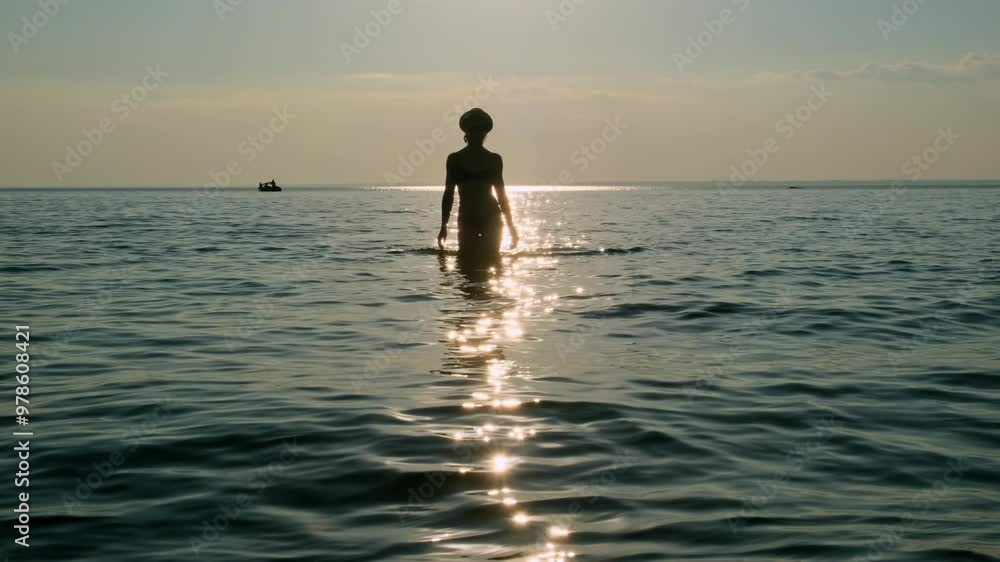 Silhouette of a young sexy woman coming out of the sea at sunset. Relaxed female tourist wearing bikini walking in the shining water enjoying beach vacation. Silhouette of a young sexy woman coming out of the sea at sunset. Relaxed female tourist wearing bikini walking in the shining water enjoying beach vacation.