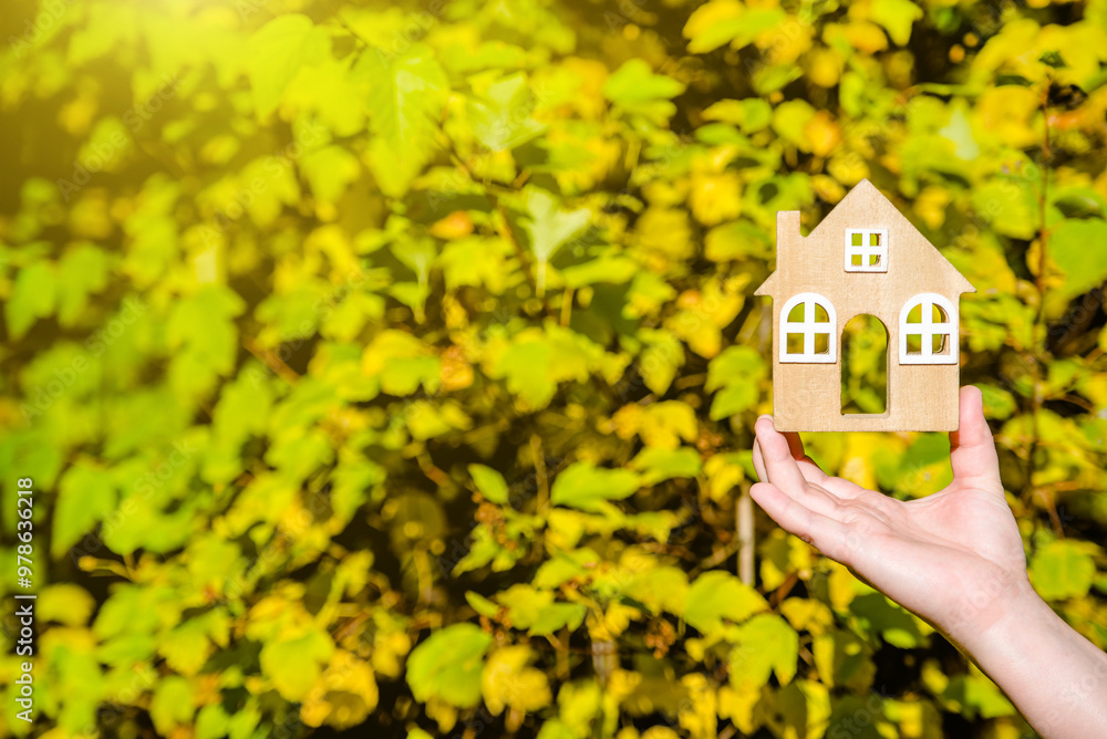 The symbol of the house in the girl's hand on the background of yellow leaves
