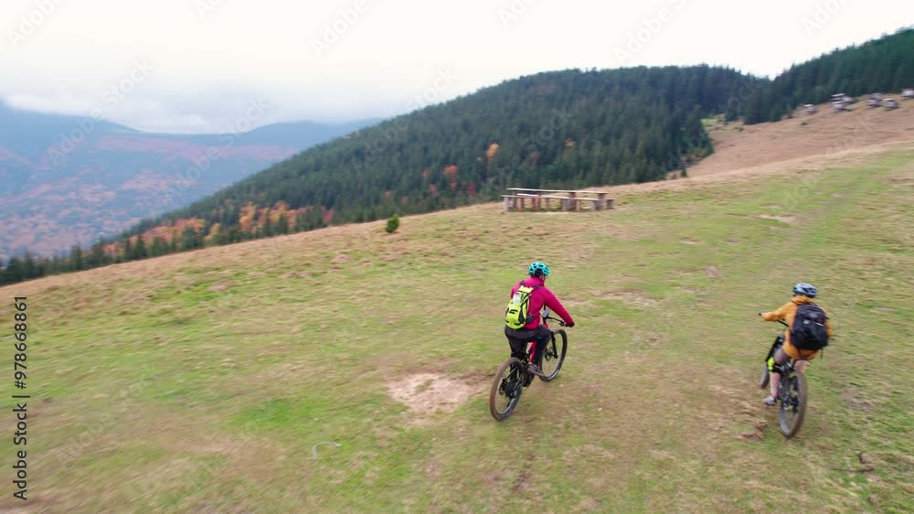 Two cyclists men riding electric bikes outdoors. Back view of male tourists biking in the mountains, wearing helmets and backpacks. Concept of sport, active leisure and nature. Two cyclists men riding electric bikes outdoors. Back view of male tourists biking in the mountains, wearing helmets and backpacks. Concept of sport, active leisure and nature.