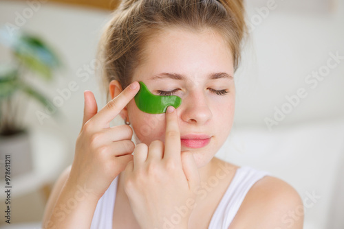 Woman applying green under-eye patch for skincare photo