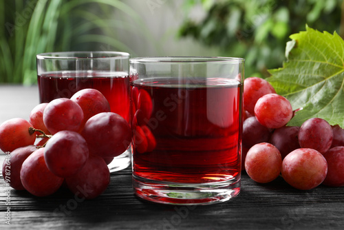 Cuadro en lienzo Tasty grape juice in glasses and berries on black wooden table against blurred g