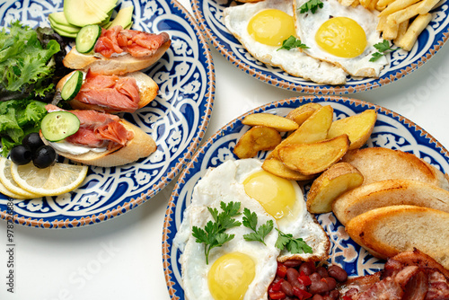 Traditional breakfast plates featuring eggs, sausages, and various accompaniments arranged artistically on a white background photo