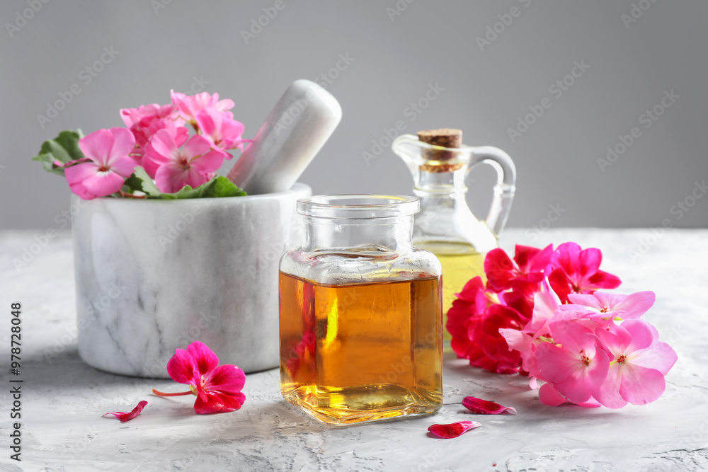 Geranium essential oil and beautiful flowers on light grey textured table Geranium essential oil and beautiful flowers on light grey textured table