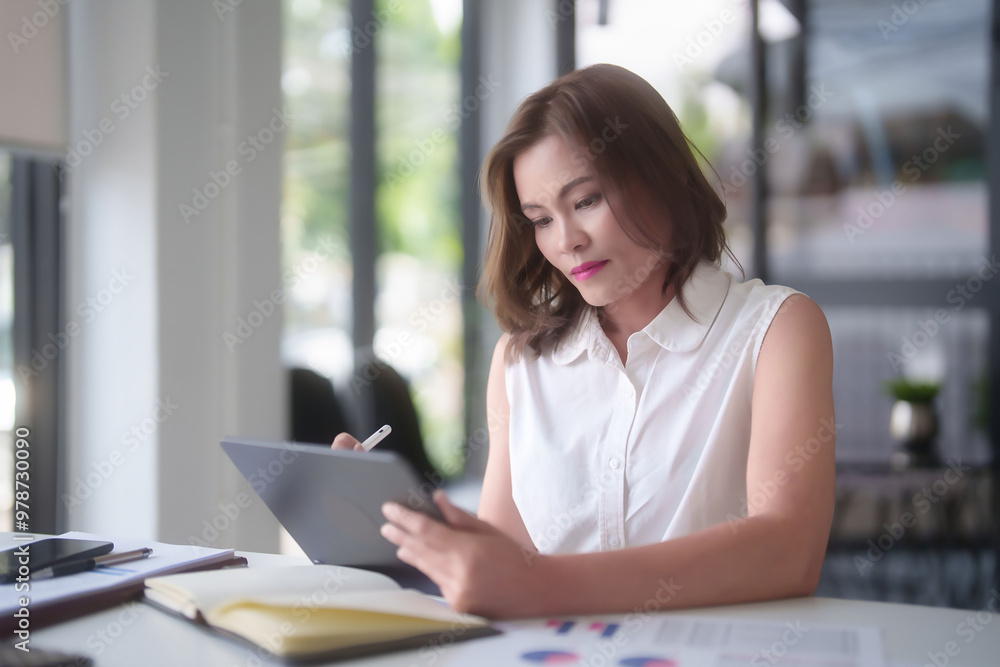 Fototapeta premium Asian businesswomen reading marketing business report to checking financial chart data on digital tablet and writing notes while analyze investment and market stock of new startup in outside office