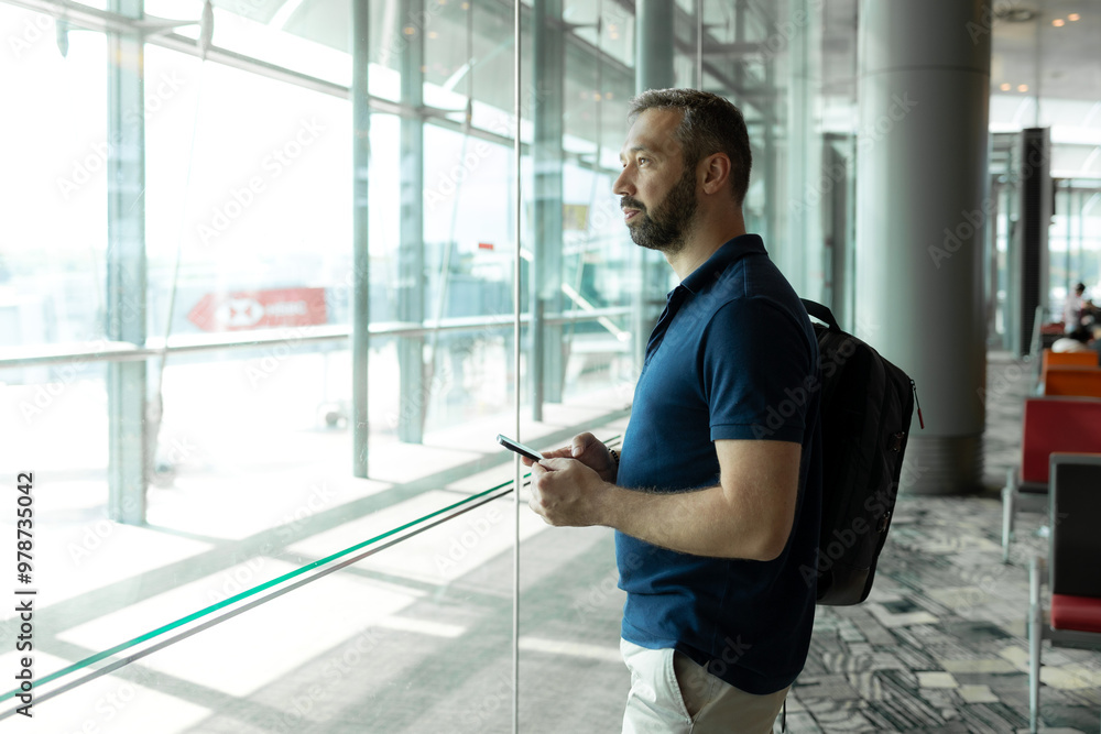 Man looks through the window while holding phone in airport Man looks through the window while holding phone in airport