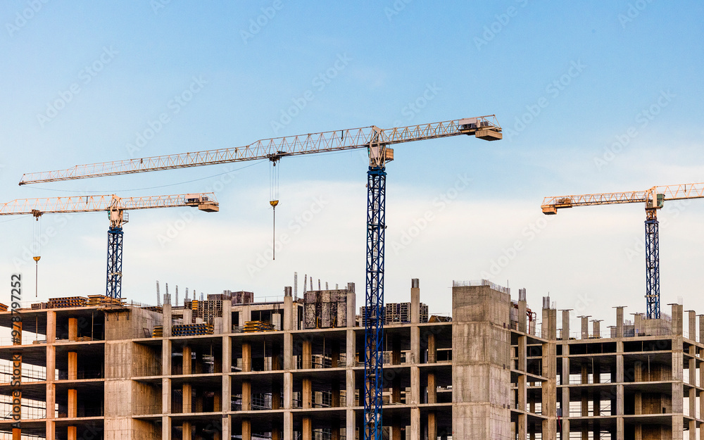 Construction cranes work on a new building in the city. Three construction cranes are seen, working to build a large concrete structure. Construction cranes work on a new building in the city. Three construction cranes are seen, working to build a large concrete structure.