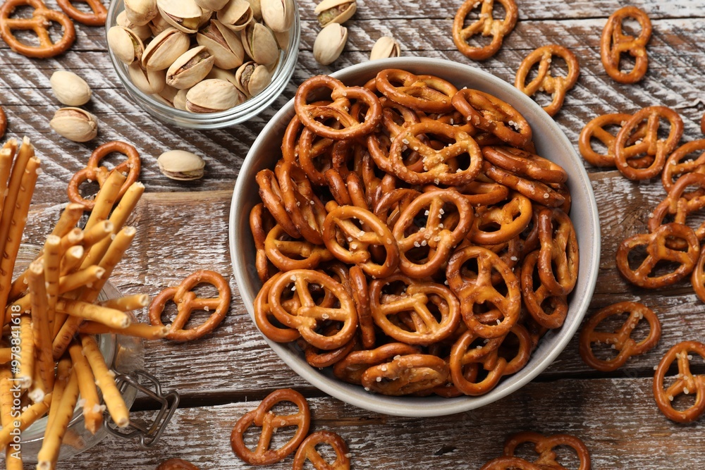 Fototapeta premium Delicious pretzel crackers, salty sticks and pistachios on wooden table, flat lay