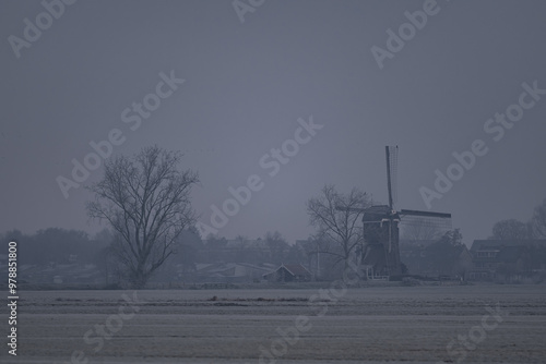 The dramatic scene with a Dutch windmill in a foggy and cold winter weather