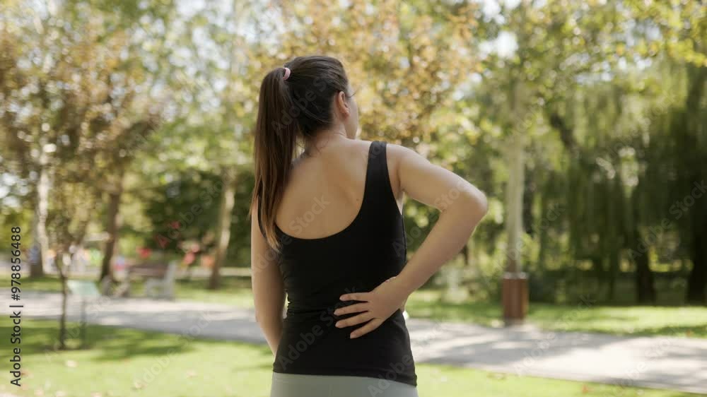 A sporty young woman encounters back pain while doing gymnastic exercises in a sunlit park A sporty young woman encounters back pain while doing gymnastic exercises in a sunlit park