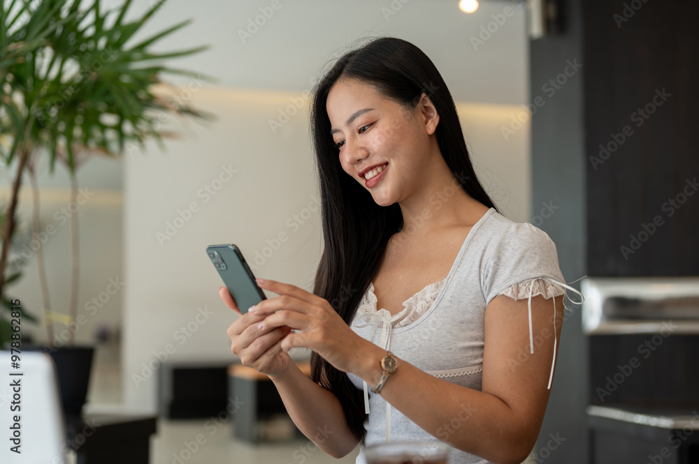 A beautiful, positive Asian woman using her smartphone while sitting in a modern coffee shop. A beautiful, positive Asian woman using her smartphone while sitting in a modern coffee shop.