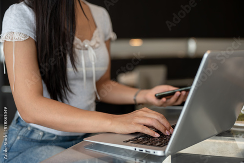 A close-up of an Asian woman working on her laptop, typing on the laptop keyboard.