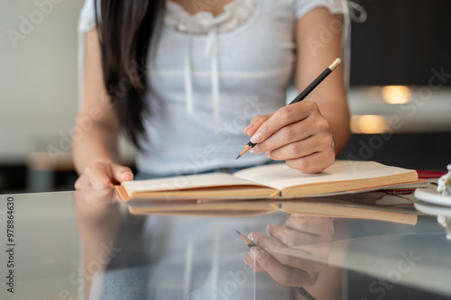 A close-up of a woman holding a pencil and writing in a book at a table indoors.