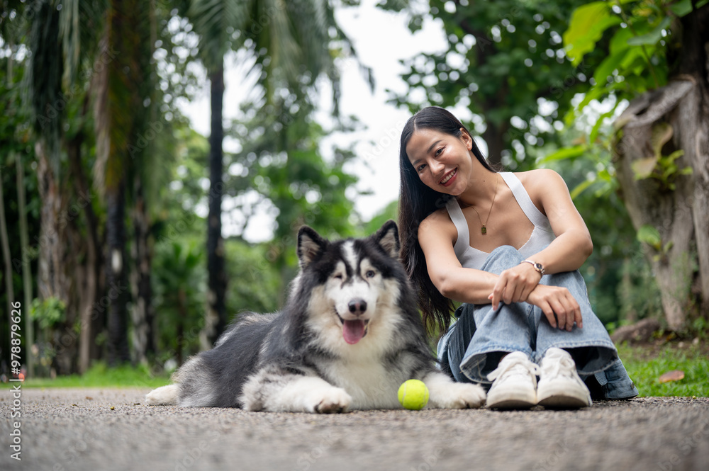 A woman smiles at the camera while sitting on a street in a park, with her dog lying nearby. A woman smiles at the camera while sitting on a street in a park, with her dog lying nearby.