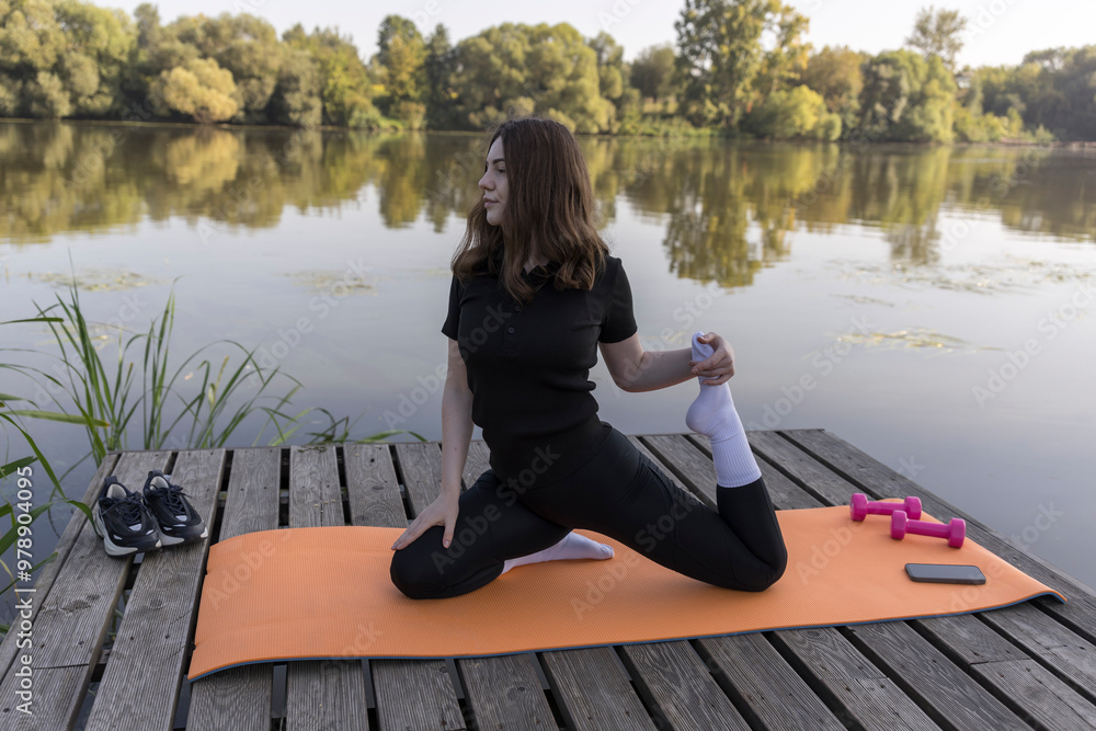 A woman is doing yoga on a mat by a lake A woman is doing yoga on a mat by a lake