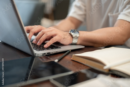 A cropped image of a man working remotely from a coffee shop, working on his laptop.