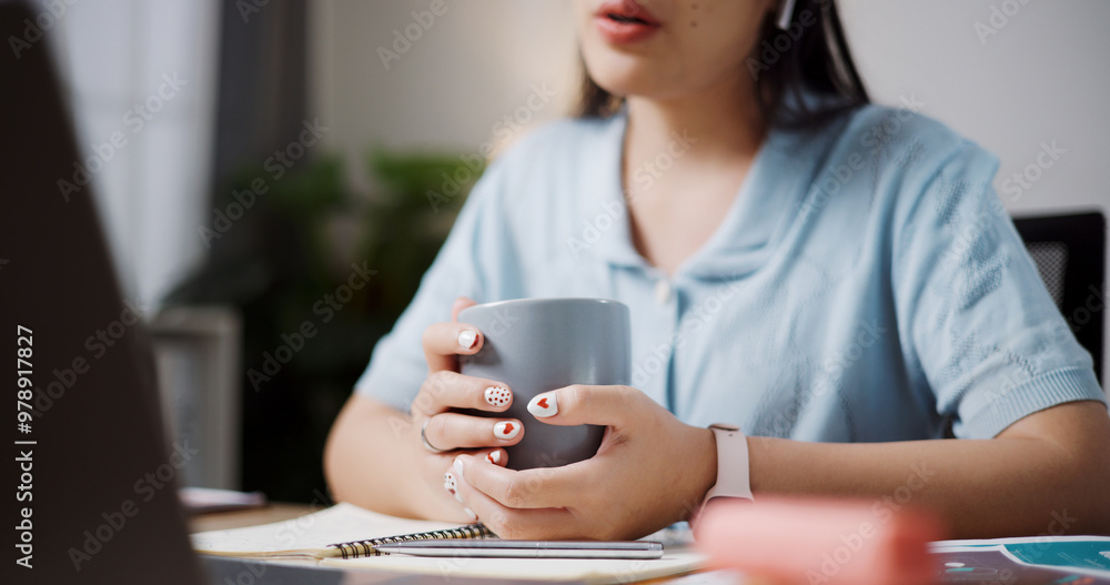 Selective focus, Hands of female freelancer holding coffee cup while explaining project in online meeting with team members via laptop in home office. Working from home, Remote working. Selective focus, Hands of female freelancer holding coffee cup while explaining project in online meeting with team members via laptop in home office. Working from home, Remote working.