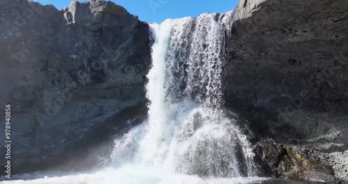 On a clear day with the sun shining bright, Waterfall Skutafoss beautifully showcases the tranquil elegance of the cascading water as it gently flows over the pebbles. photo