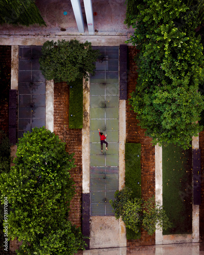 Aerial view of a peaceful urban garden with a woman walking along a pathway surrounded by greenery and modern apartments at sunrise, Cyberjaya, Malaysia.