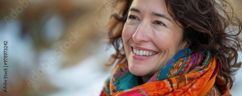 A smiling woman with a colorful scarf poses against a winter scene, exuding warmth and happiness.