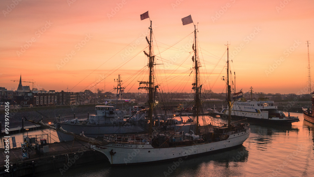 Harlingen, Netherlands - 25 February 2021: Aerial view of the tranquil port with the tall ship Bark Europa at sunrise, Harlingen, Netherlands. Harlingen, Netherlands - 25 February 2021: Aerial view of the tranquil port with the tall ship Bark Europa at sunrise, Harlingen, Netherlands.