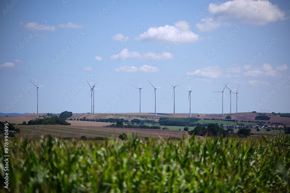 Green cornfield and wind power turbine against a blue sky with white clouds. Renewable energy source. Powerful and ecological energy concept