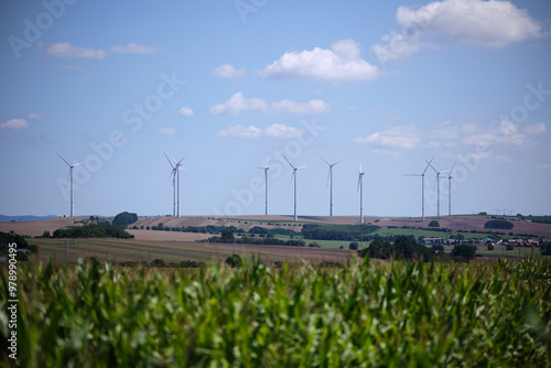 Obraz na płótnie Green cornfield and wind power turbine against a blue sky with white clouds. Renewable energy source. Powerful and ecological energy concept w salonie