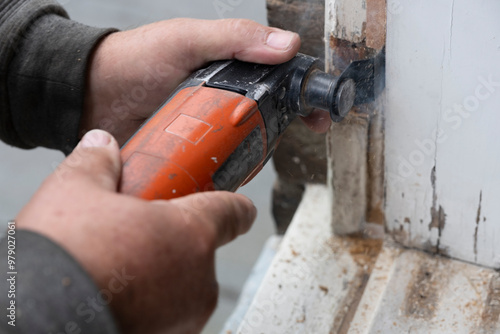 Fotografie Carpenter cuts a piece of rotten wood from a window frame with an oscillating re